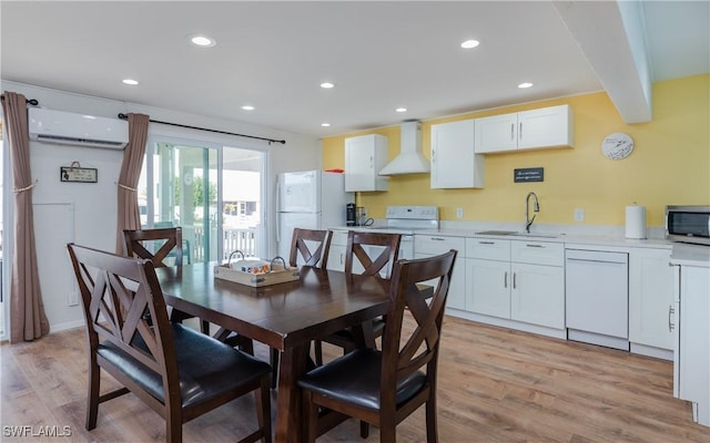 dining area featuring sink, a wall unit AC, beamed ceiling, and light wood-type flooring