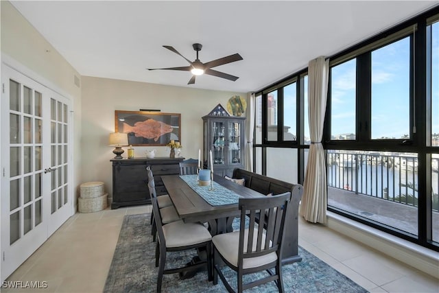 tiled dining room featuring expansive windows, a water view, ceiling fan, and french doors