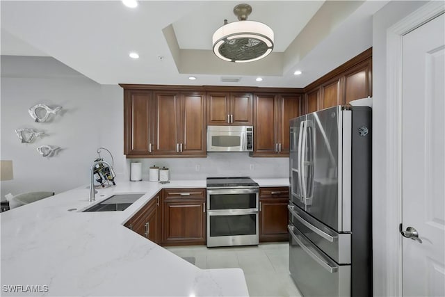 kitchen featuring appliances with stainless steel finishes, kitchen peninsula, sink, a tray ceiling, and light stone countertops