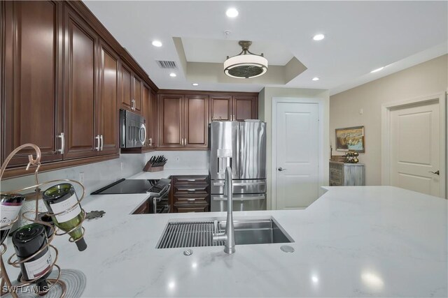 kitchen with light stone counters, stainless steel appliances, a raised ceiling, and kitchen peninsula