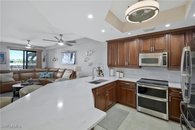 kitchen with sink, appliances with stainless steel finishes, light stone counters, light tile patterned flooring, and kitchen peninsula