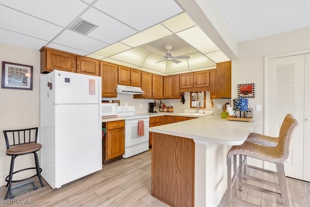 kitchen featuring a breakfast bar area, white appliances, ceiling fan, kitchen peninsula, and light wood-type flooring