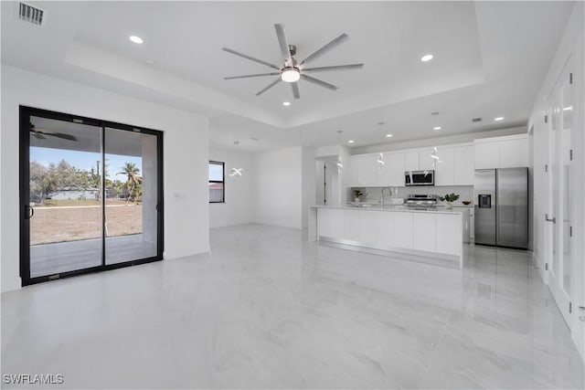 kitchen featuring ceiling fan, white cabinetry, stainless steel appliances, a tray ceiling, and decorative backsplash