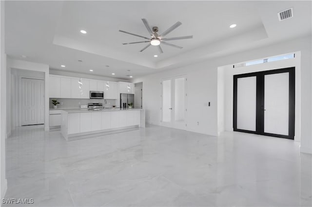 unfurnished living room with a tray ceiling, french doors, and ceiling fan