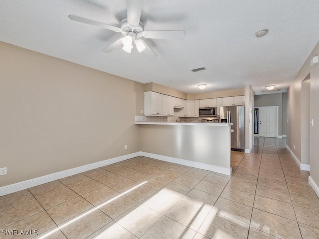 kitchen with light tile patterned floors, kitchen peninsula, ceiling fan, stainless steel appliances, and white cabinets