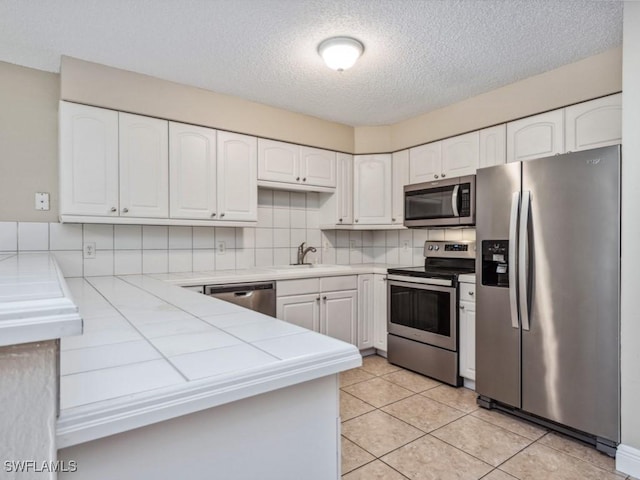 kitchen with appliances with stainless steel finishes, tile countertops, sink, white cabinets, and decorative backsplash