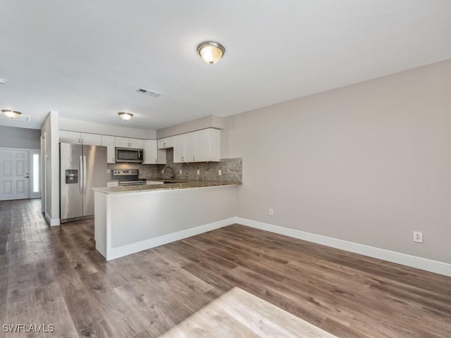 kitchen featuring hardwood / wood-style flooring, appliances with stainless steel finishes, white cabinets, decorative backsplash, and kitchen peninsula