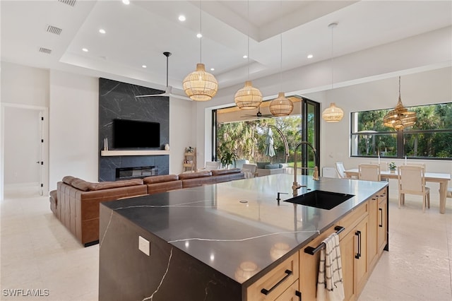 kitchen with sink, a tray ceiling, a fireplace, light brown cabinetry, and a large island with sink