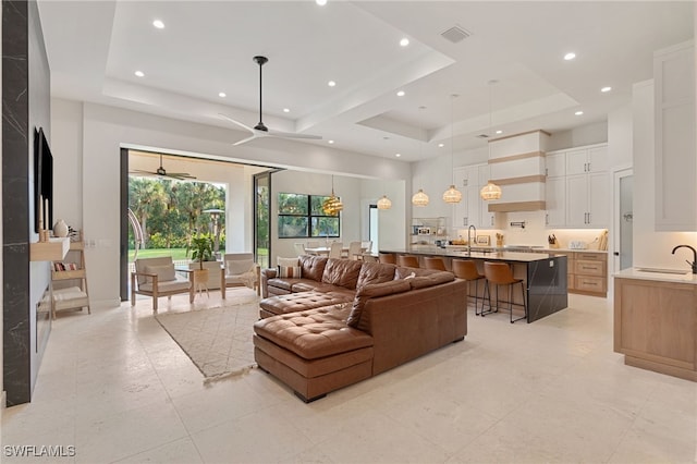 living room with ceiling fan, a tray ceiling, and sink