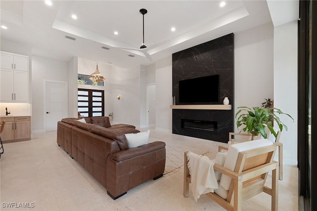 living room with a tray ceiling, a high end fireplace, and a towering ceiling