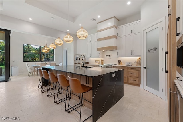 kitchen featuring sink, a large island with sink, a tray ceiling, pendant lighting, and white cabinets