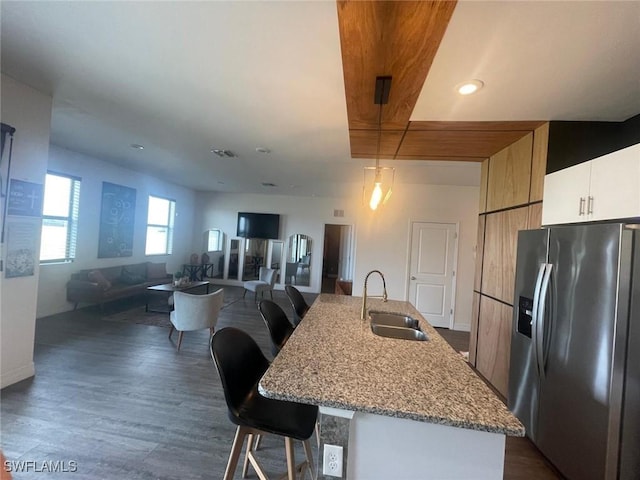 kitchen with stainless steel refrigerator with ice dispenser, sink, a breakfast bar area, a kitchen island with sink, and white cabinets