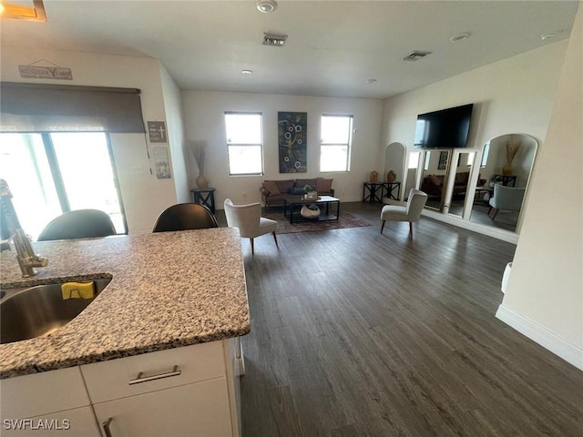 kitchen with sink, dark wood-type flooring, light stone countertops, white cabinets, and a kitchen island