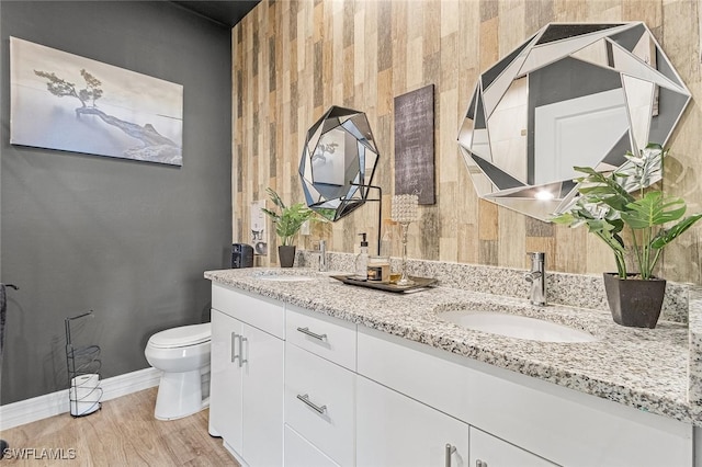 full bathroom with toilet, baseboards, a sink, double vanity, and wood finished floors