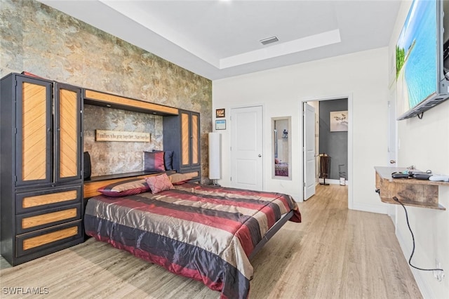 bedroom featuring baseboards, visible vents, a tray ceiling, and wood finished floors