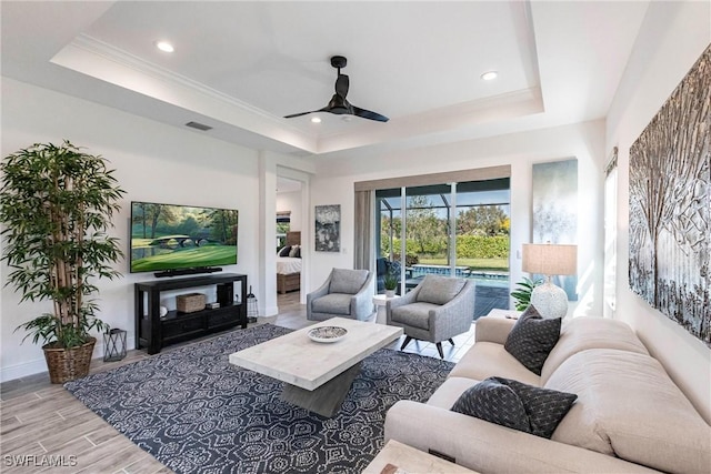 living room with a raised ceiling, ornamental molding, ceiling fan, and light hardwood / wood-style floors