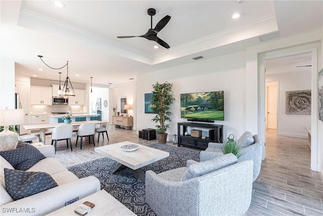 living room with a raised ceiling, crown molding, and ceiling fan