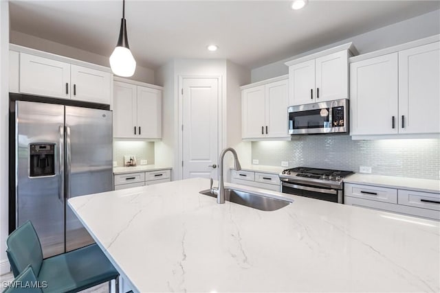 kitchen featuring appliances with stainless steel finishes, light stone countertops, white cabinetry, pendant lighting, and a sink