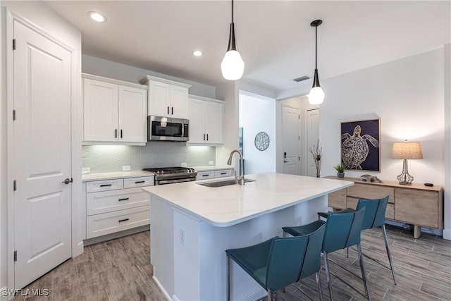 kitchen with decorative light fixtures, appliances with stainless steel finishes, a kitchen island with sink, white cabinets, and a sink