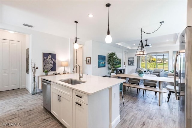 kitchen featuring visible vents, appliances with stainless steel finishes, white cabinetry, a sink, and an island with sink