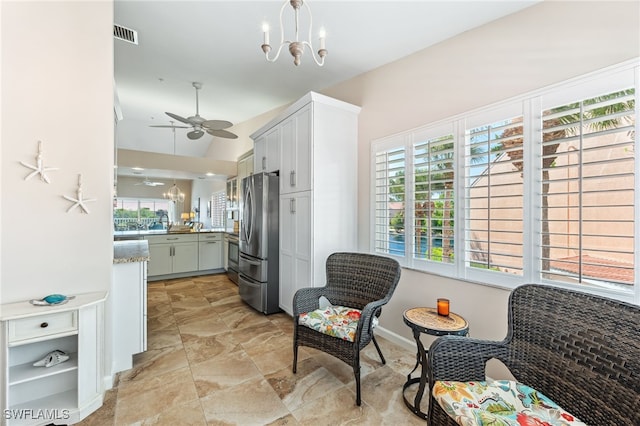 kitchen featuring stainless steel refrigerator, white cabinetry, light stone countertops, ceiling fan with notable chandelier, and kitchen peninsula