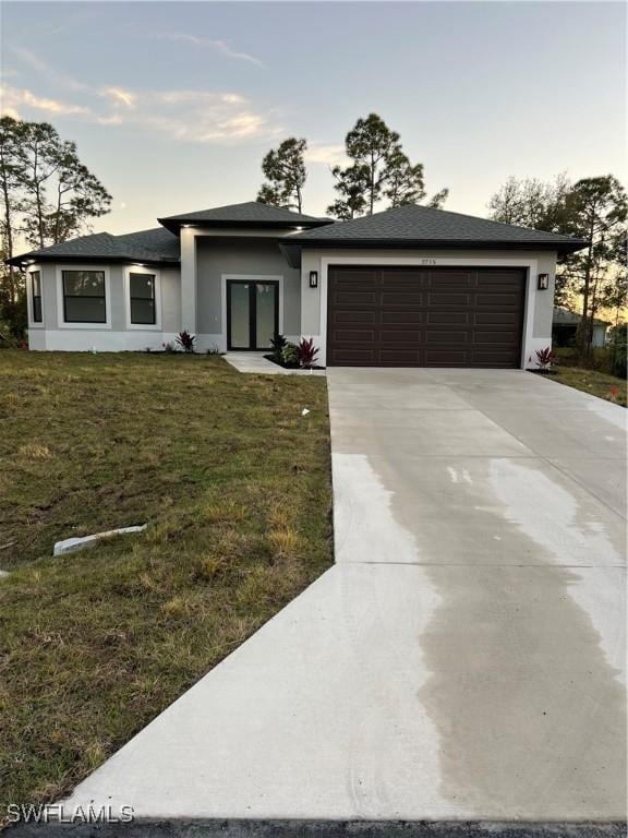 prairie-style home with a garage, driveway, a front yard, and stucco siding