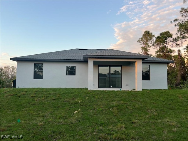 back of property featuring a shingled roof, a lawn, and stucco siding