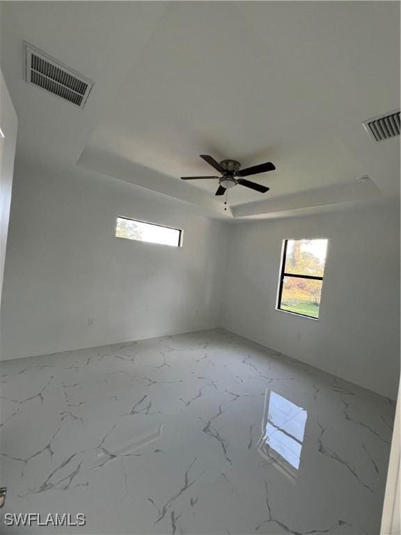 empty room featuring a ceiling fan, a tray ceiling, marble finish floor, and visible vents