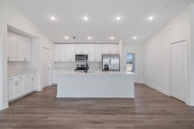 kitchen featuring appliances with stainless steel finishes, white cabinetry, an island with sink, dark hardwood / wood-style flooring, and vaulted ceiling