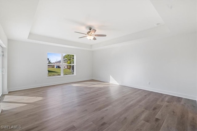 empty room featuring wood-type flooring, a raised ceiling, and ceiling fan