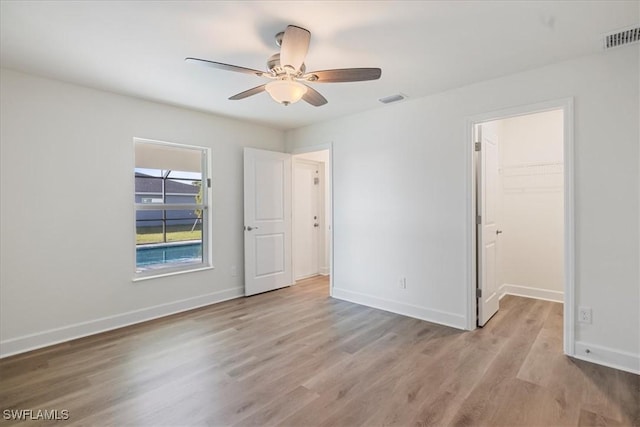 unfurnished bedroom with ceiling fan, a walk in closet, light hardwood / wood-style floors, and a closet