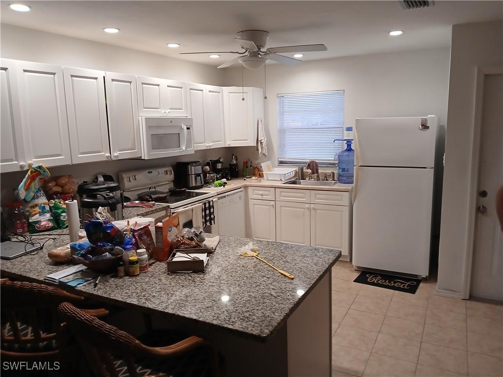 kitchen with sink, white cabinets, light stone counters, kitchen peninsula, and white appliances