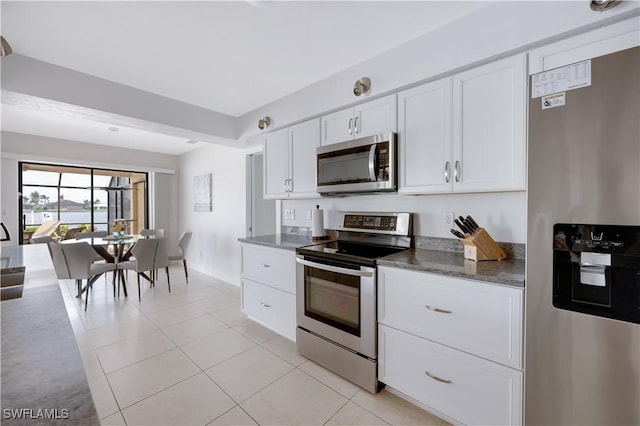 kitchen with appliances with stainless steel finishes, light tile patterned floors, white cabinets, and dark stone counters