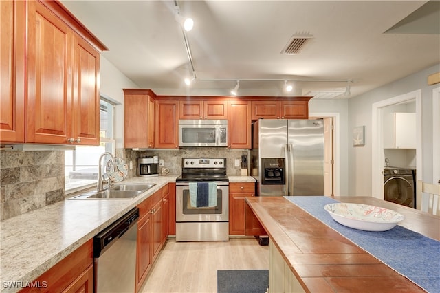 kitchen featuring appliances with stainless steel finishes, washer / dryer, sink, backsplash, and light hardwood / wood-style floors