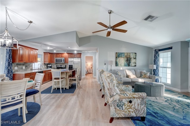 living room with vaulted ceiling, ceiling fan with notable chandelier, and light wood-type flooring