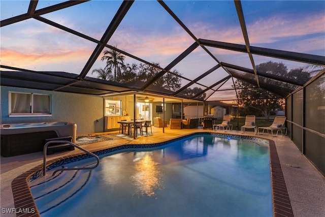 pool at dusk featuring a hot tub, glass enclosure, and a patio area