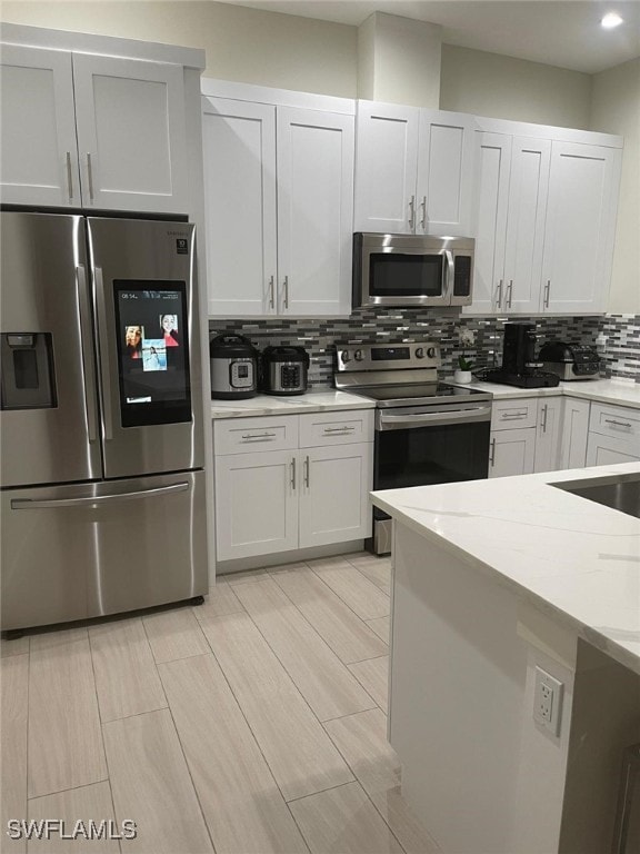 kitchen featuring appliances with stainless steel finishes, light stone counters, white cabinets, and backsplash