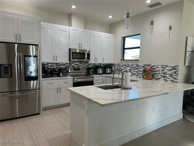 kitchen with appliances with stainless steel finishes, decorative light fixtures, white cabinetry, kitchen peninsula, and light stone countertops