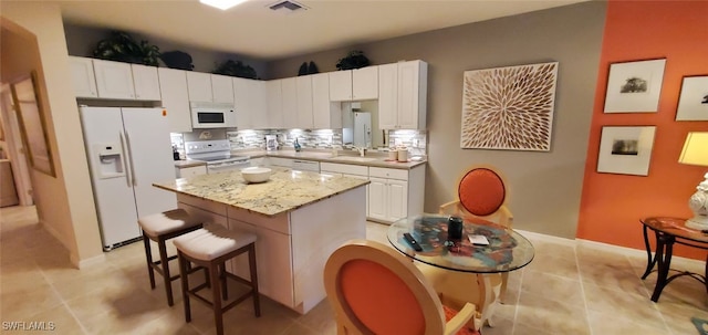 kitchen featuring light stone counters, a kitchen island, white appliances, decorative backsplash, and white cabinets