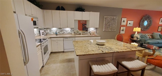 kitchen featuring white appliances, a breakfast bar, white cabinetry, tasteful backsplash, and a kitchen island