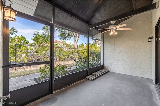 unfurnished sunroom featuring beamed ceiling and ceiling fan