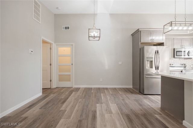 kitchen with hanging light fixtures, appliances with stainless steel finishes, hardwood / wood-style flooring, and gray cabinetry