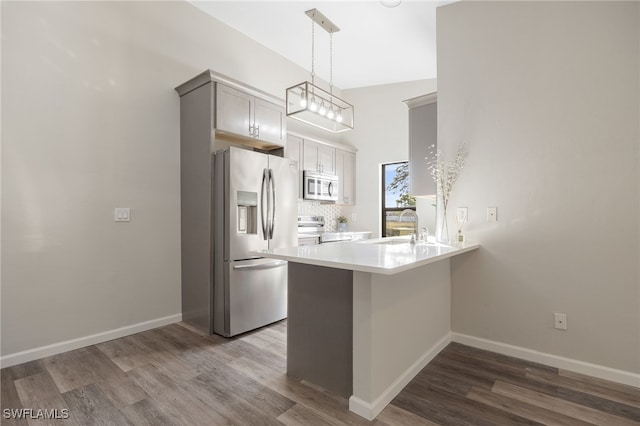 kitchen featuring sink, dark hardwood / wood-style flooring, kitchen peninsula, pendant lighting, and stainless steel appliances