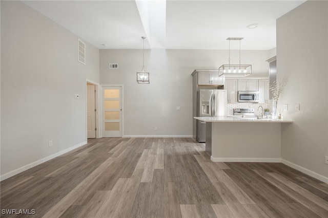 kitchen featuring appliances with stainless steel finishes, hanging light fixtures, tasteful backsplash, dark hardwood / wood-style flooring, and kitchen peninsula