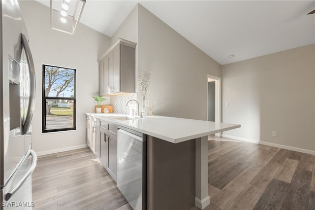 kitchen with appliances with stainless steel finishes, a kitchen bar, gray cabinets, and light wood-type flooring