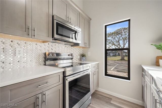 kitchen with gray cabinetry, light wood-type flooring, tasteful backsplash, and appliances with stainless steel finishes