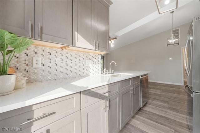 kitchen with sink, backsplash, stainless steel appliances, decorative light fixtures, and light wood-type flooring