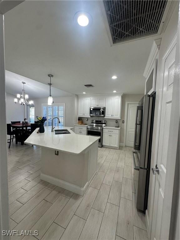 kitchen featuring sink, white cabinetry, hanging light fixtures, stainless steel appliances, and a center island with sink