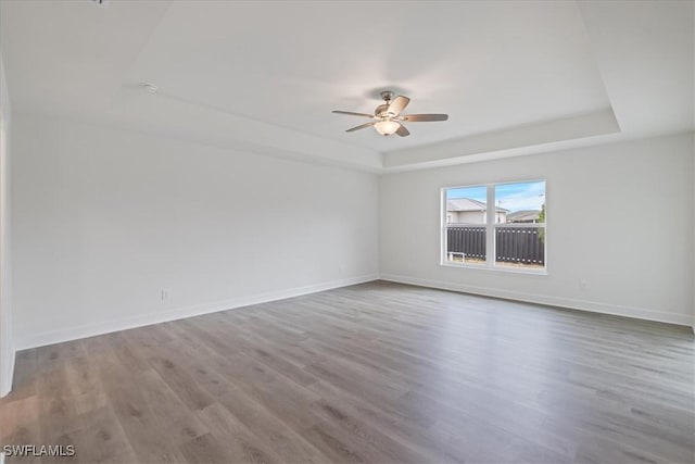 unfurnished room featuring a raised ceiling, wood-type flooring, and ceiling fan