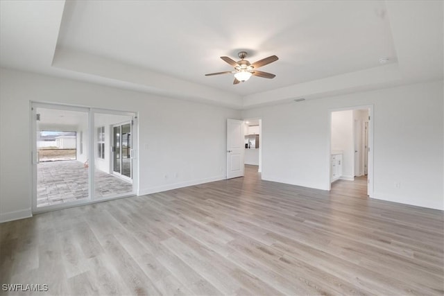 unfurnished room with ceiling fan, light wood-type flooring, and a tray ceiling